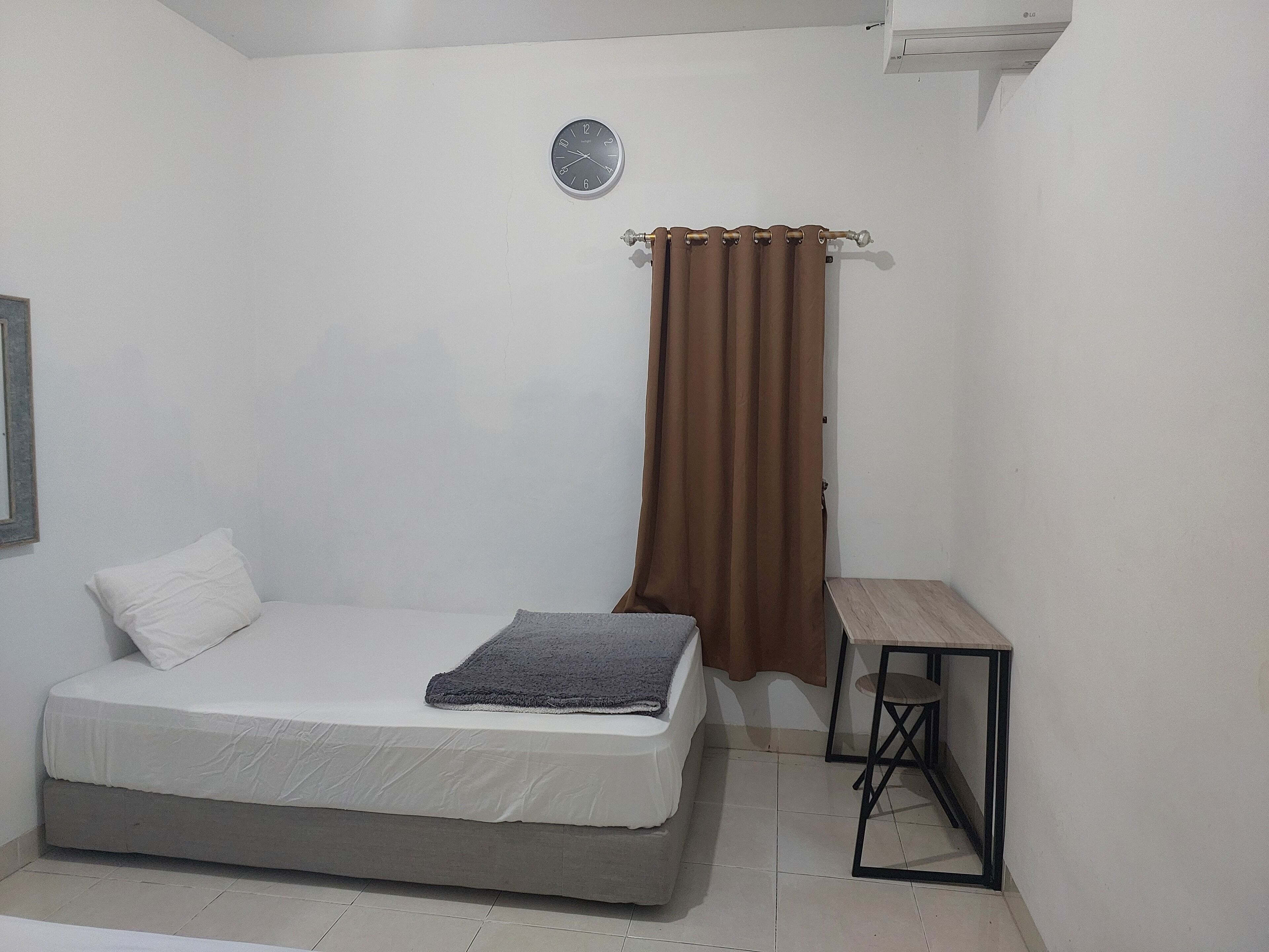 A small, clean room with a bed, a small table, and a wall-mounted air conditioning unit.