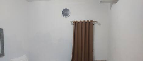 A small, clean room with a bed, a small table, and a wall-mounted air conditioning unit.