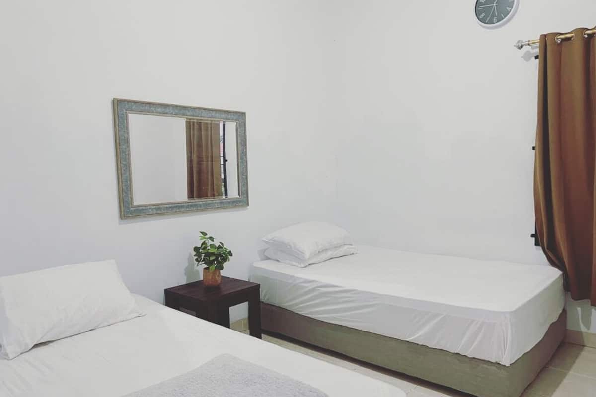 Ein Zimmer mit zwei Betten, einem kleinen Tisch mit Pflanze, einem Spiegel an der Wand und einer Uhr.