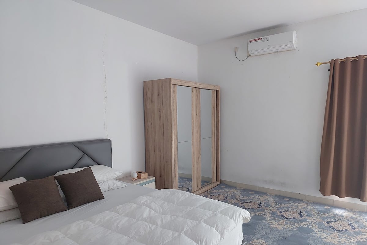 Ein Schlafzimmer mit einem Bett, einem Kleiderschrank, einem Nachttisch und einem gemusterten Teppich.