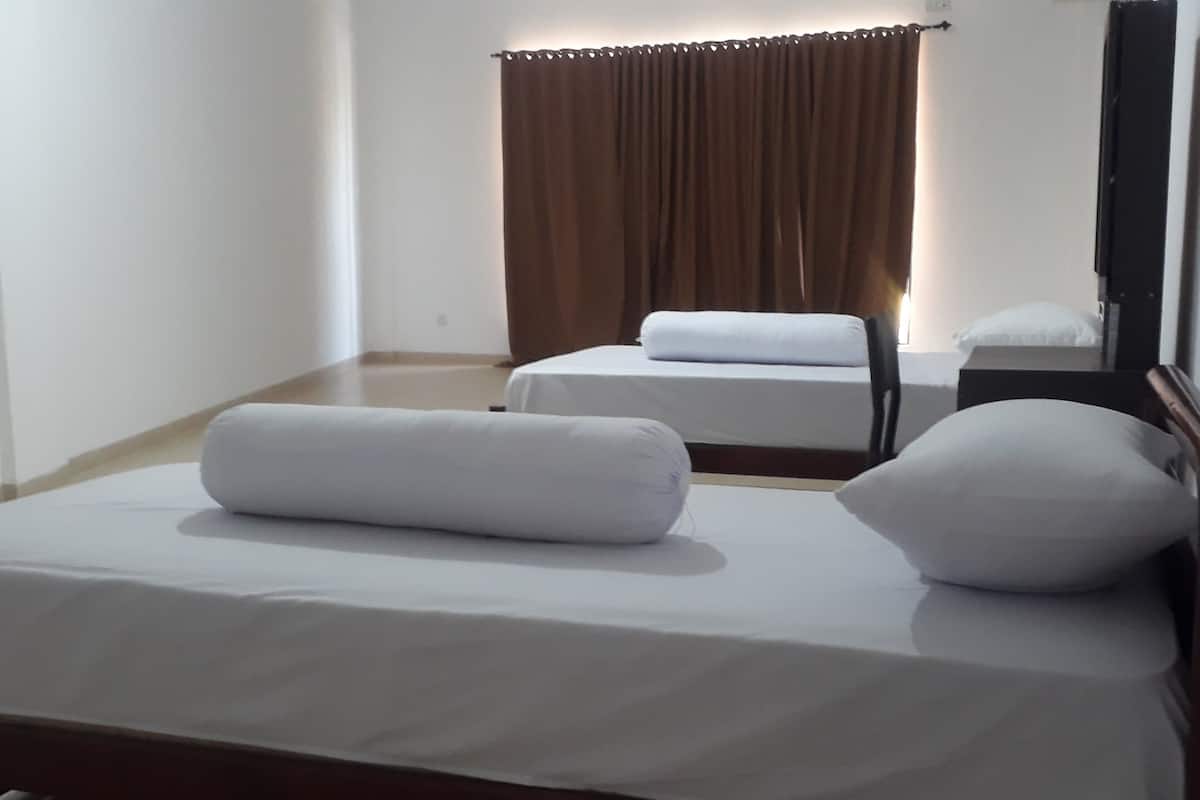 Ein Hotelzimmer mit zwei Betten, einem Fenster mit braunen Vorhängen und einem Spiegel an der Wand.