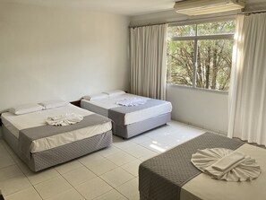 Quarto de hotel com duas camas, uma mesinha e uma janela com cortinas.