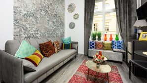 A living room with a grey sofa, colorful cushions, a red patterned rug, and a window with curtains. - Native Apartments Studencka 25 (Kraków)