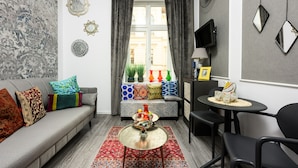 A living room with a grey sofa, colorful cushions, a round coffee table, and a window with curtains. - Native Apartments Studencka 25 (Kraków)