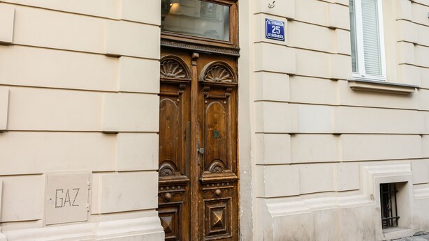 A building with a large wooden double door, a blue sign with the number 25, and a small window with white shutters. - Native Apartments Studencka 25 (Kraków)