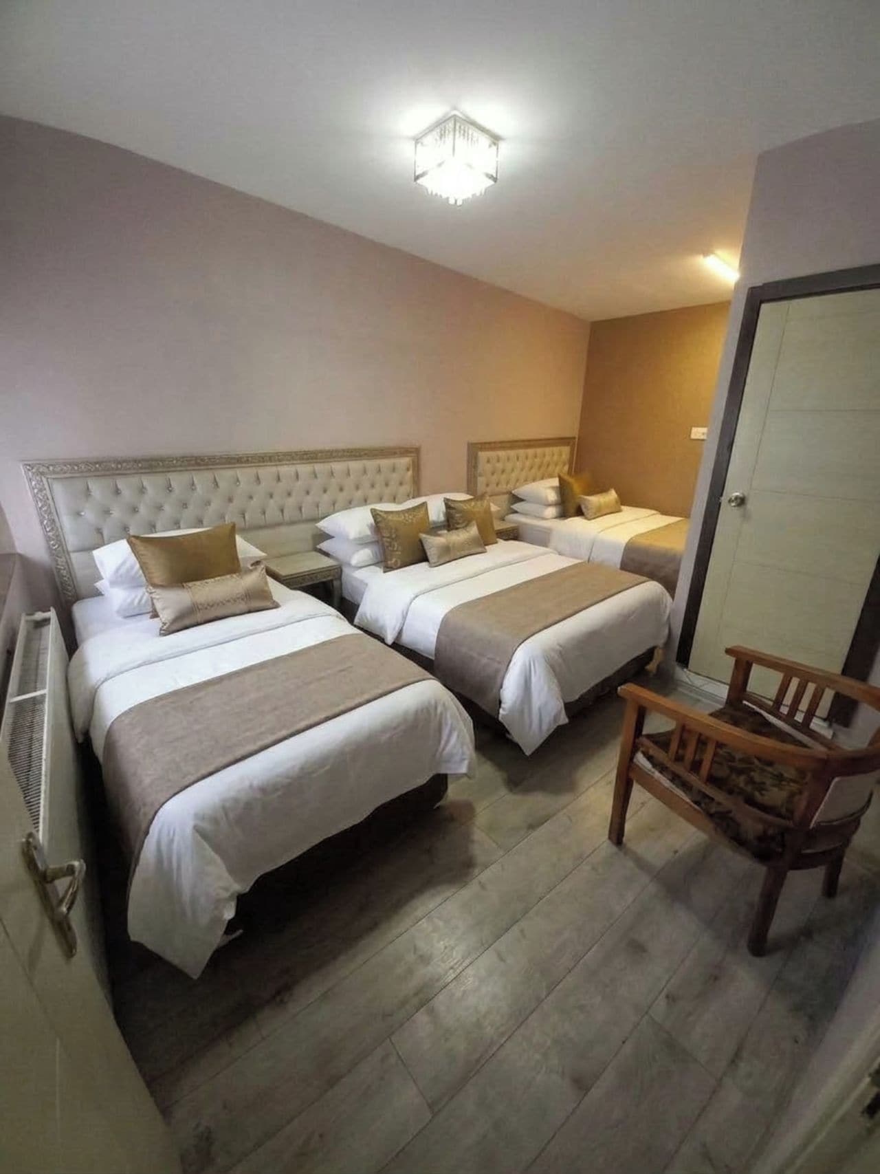 Une chambre d’hôtel avec deux lits, une chaise en bois et un radiateur.