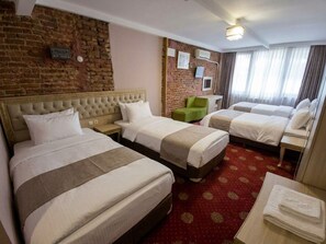 A hotel room with three beds, a brick wall, and a red carpet. - Şenkol Hotel (Ipsala)