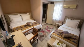 Een hotelkamer met twee bedden, een bureau met een computer, een stoel, een klein tafeltje met toiletartikelen en een badkamers deur.