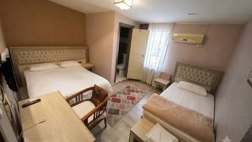 A hotel room with two beds, a desk, a chair, a small table, and a bathroom.
