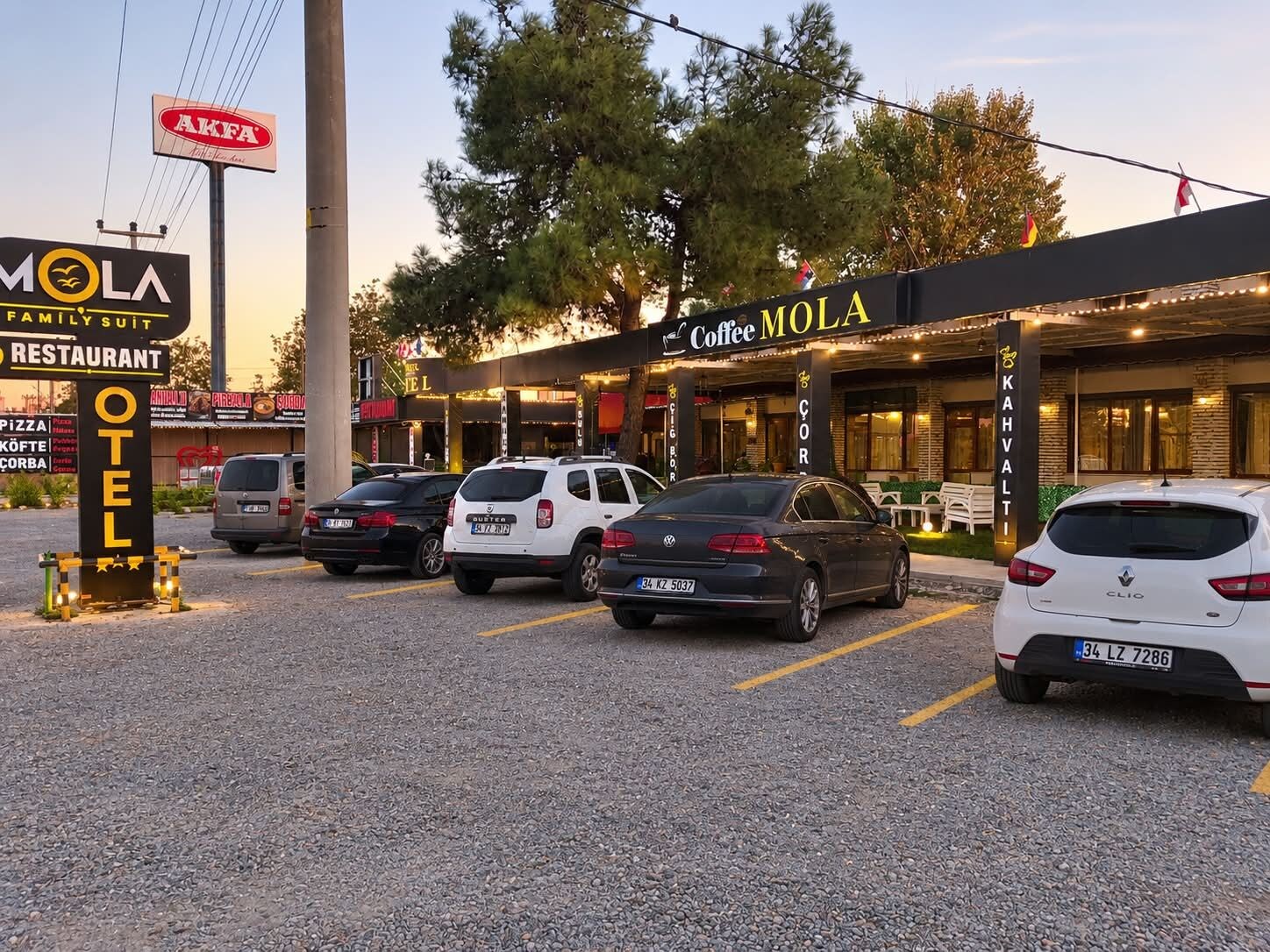 A parking lot with several cars, a coffee shop named 'Coffee MOLA,' and a sign for 'AKFA.'