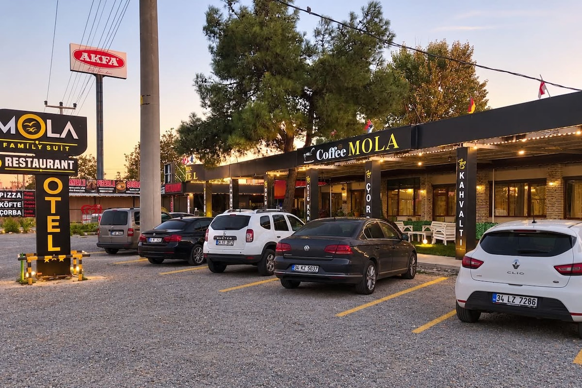 Un estacionamiento con varios autos, una cafetería llamada 'Coffee MOLA' y un letrero que dice 'AKFA'.