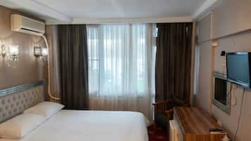A hotel room with a bed, a desk, a television, and an air conditioning unit.