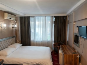 Una habitación de hotel con cama, escritorio, televisor y aire acondicionado.
