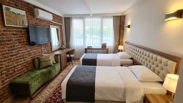 A hotel room with a brick wall, a flat-screen TV, two beds, a sofa, a desk, and a window with curtains.