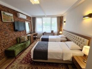 A hotel room with a brick wall, a flat-screen TV, two beds, a sofa, a desk, and a window with curtains. - Şenkol Hotel (Ipsala)
