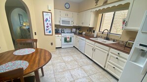 A kitchen with white cabinets, a microwave, a stove, and a sink. There is a clock on the wall and a framed picture of chili peppers. - Green Valley Casita - View ! (Green Valley)