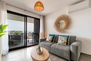A modern living room with a grey sofa, a round wooden coffee table, and a large window with a view of the outdoors. - Dieu Nérée & its sea view (Sète)
