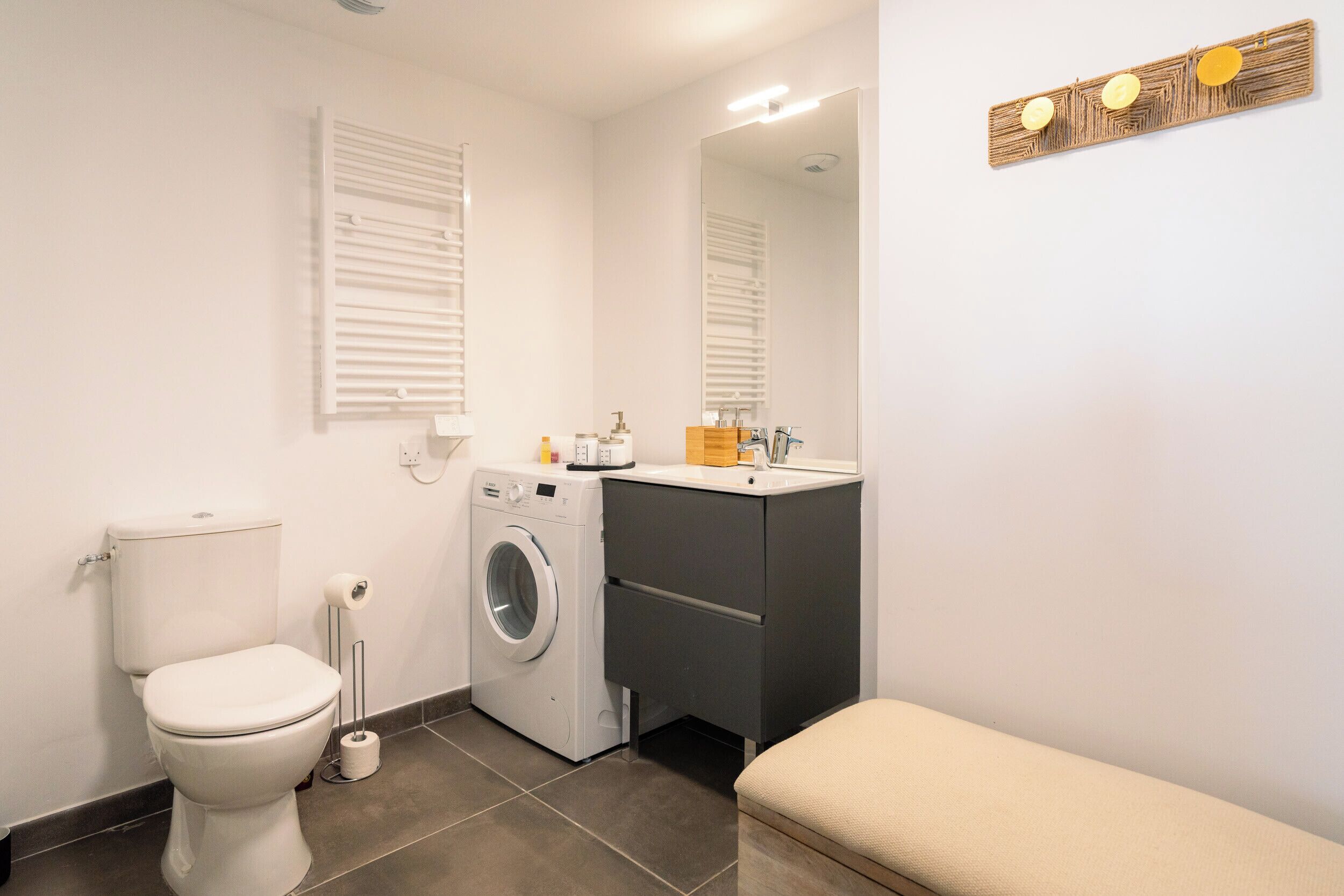 Une petite salle de bain comprenant des toilettes, un lave-linge, un lavabo et un banc.