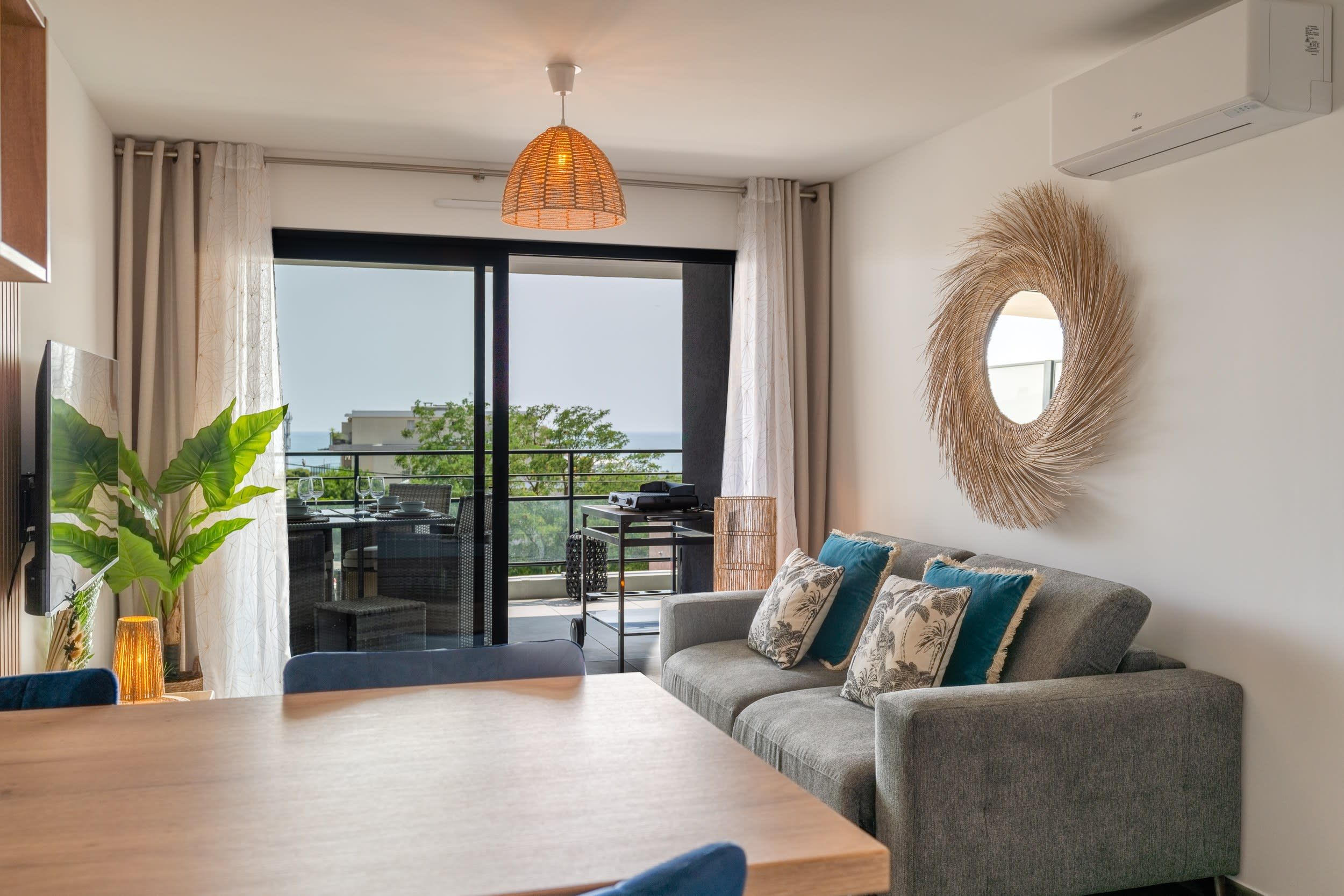 A modern living room with a sofa, a dining table, and a view through a glass door to an outdoor area.