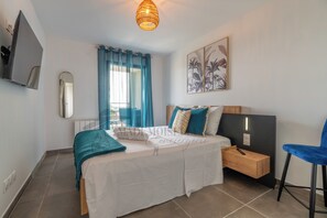 A modern bedroom with a bed, a bedside table, a chair, a TV, and a window with curtains. - Dieu Nérée & its sea view (Sète)