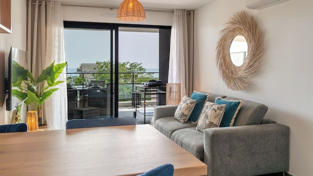 A modern living room with a sofa, a dining table, and a view through a glass door to an outdoor area with a table and chairs. - Dieu Nérée & its sea view (Sète)