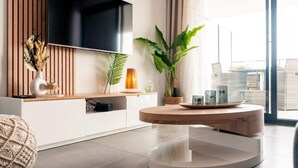 A modern living room with a flat-screen TV mounted on a wooden wall, a round coffee table, and a large potted plant. - Dieu Nérée & its sea view (Sète)