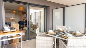 A modern dining area with a glass partition, wicker furniture, and a view of the kitchen and living space. - Dieu Nérée & its sea view (Sète)