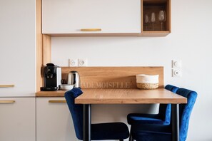 A modern kitchen with a wooden table, two blue chairs, a coffee maker, a kettle, and a woven basket. - Dieu Nérée & its sea view (Sète)