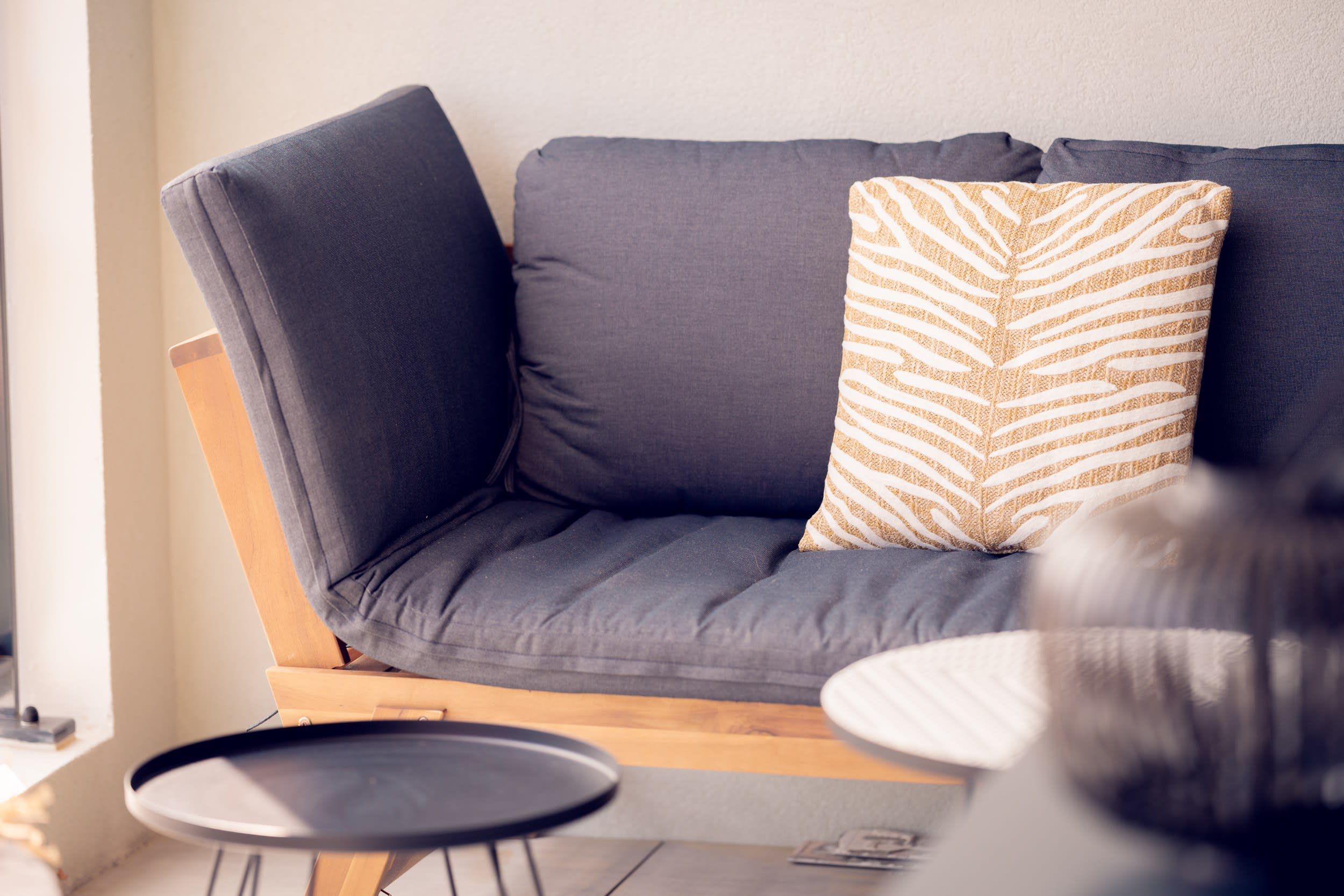 A modern living area with a grey sofa, a patterned throw pillow, and a small round table.