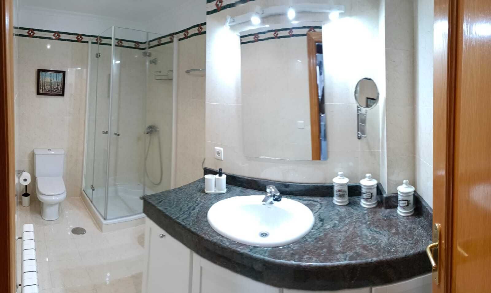 A bathroom with a glass-enclosed shower, a white sink with a marble countertop, and a large mirror above the sink.
