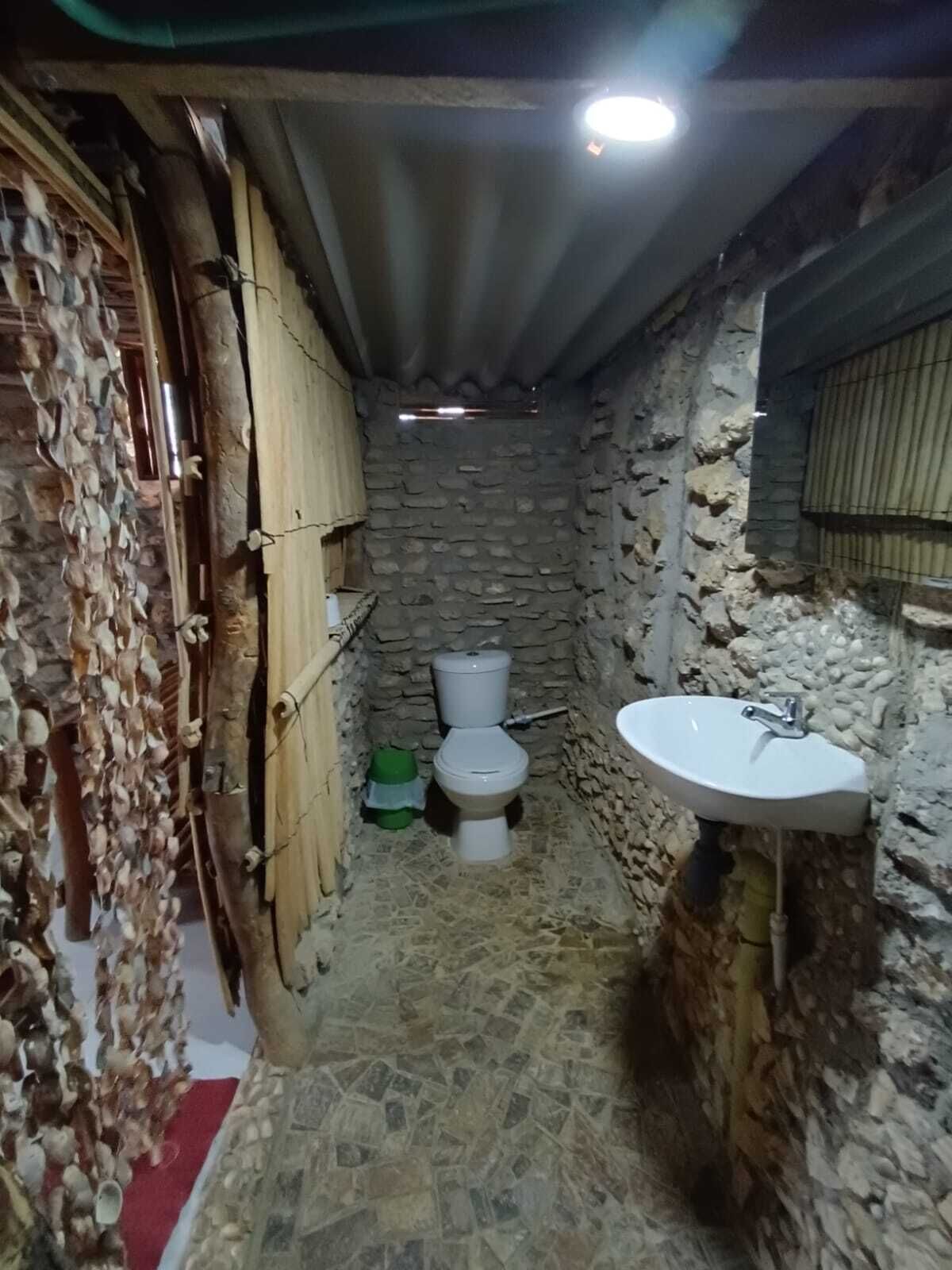 Un baño pequeño y rústico con pared de piedra, un inodoro y un lavamanos.