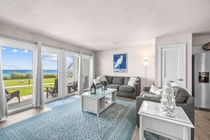 A living room with a view of the sea, a gray sofa, a coffee table, and a patterned rug.