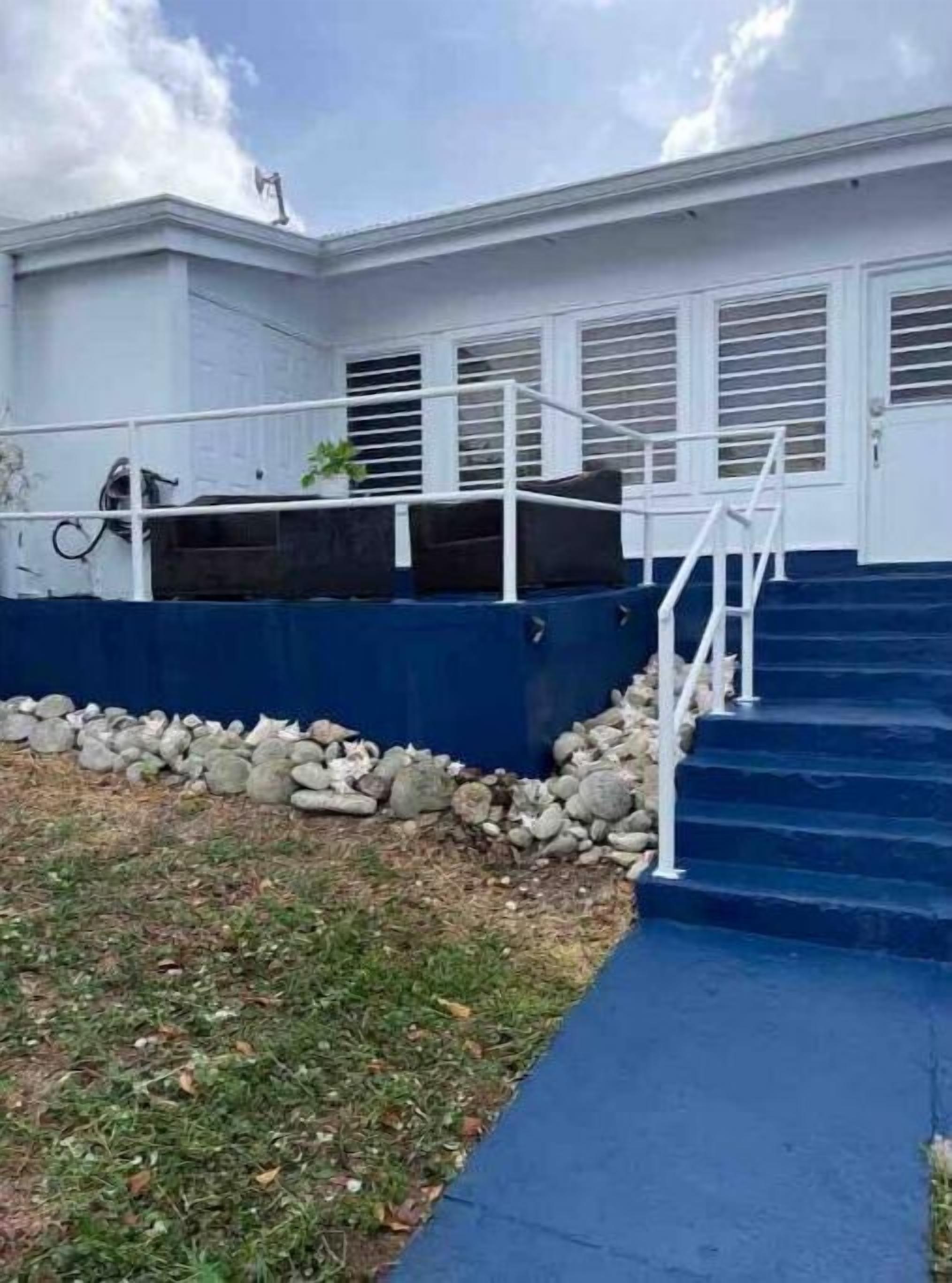 Un edificio con una scala che conduce a una porta, una piccola zona giardino con rocce e un sentiero blu.