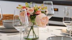A dining table set with plates, bowls, glasses, and a vase with flowers.
