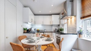 A modern kitchen with white cabinets, a round dining table with wicker chairs, and a window with blinds.