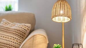 A round white nightstand with a woven lamp, a small potted plant, and a black candle holder.