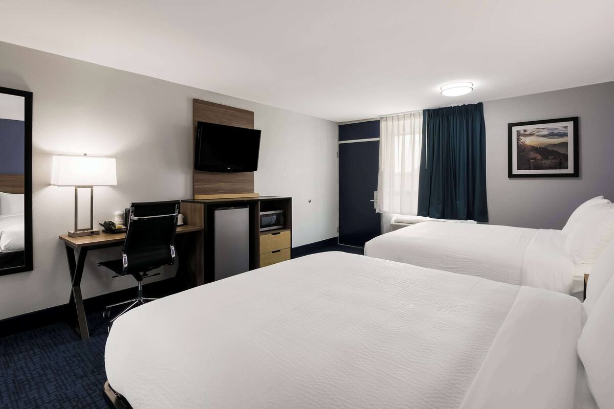 Een hotelkamer met twee bedden, een bureau met stoel, een televisie en een raam met gordijnen.