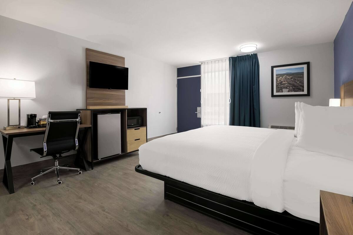 Een hotelkamer met een bed, bureau, stoel, televisie en een raam met gordijnen.
