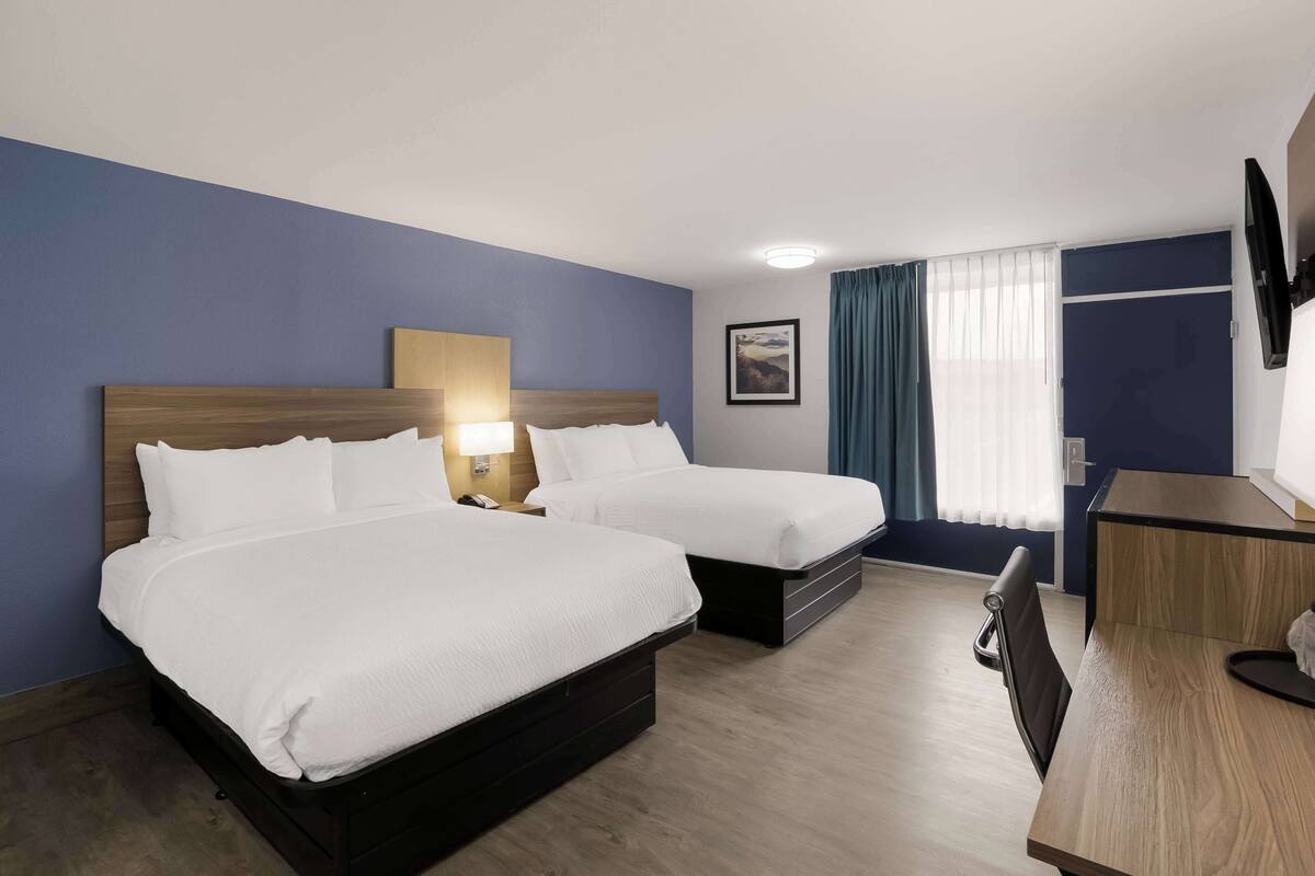 Een hotelkamer met twee bedden, een bureau, een stoel, een televisie en een raam met gordijnen.