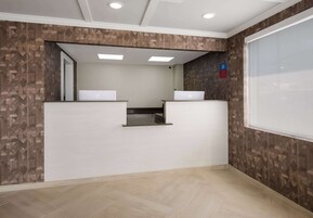 A reception area with a modern design, featuring a patterned wall, a reception desk, and a large window.