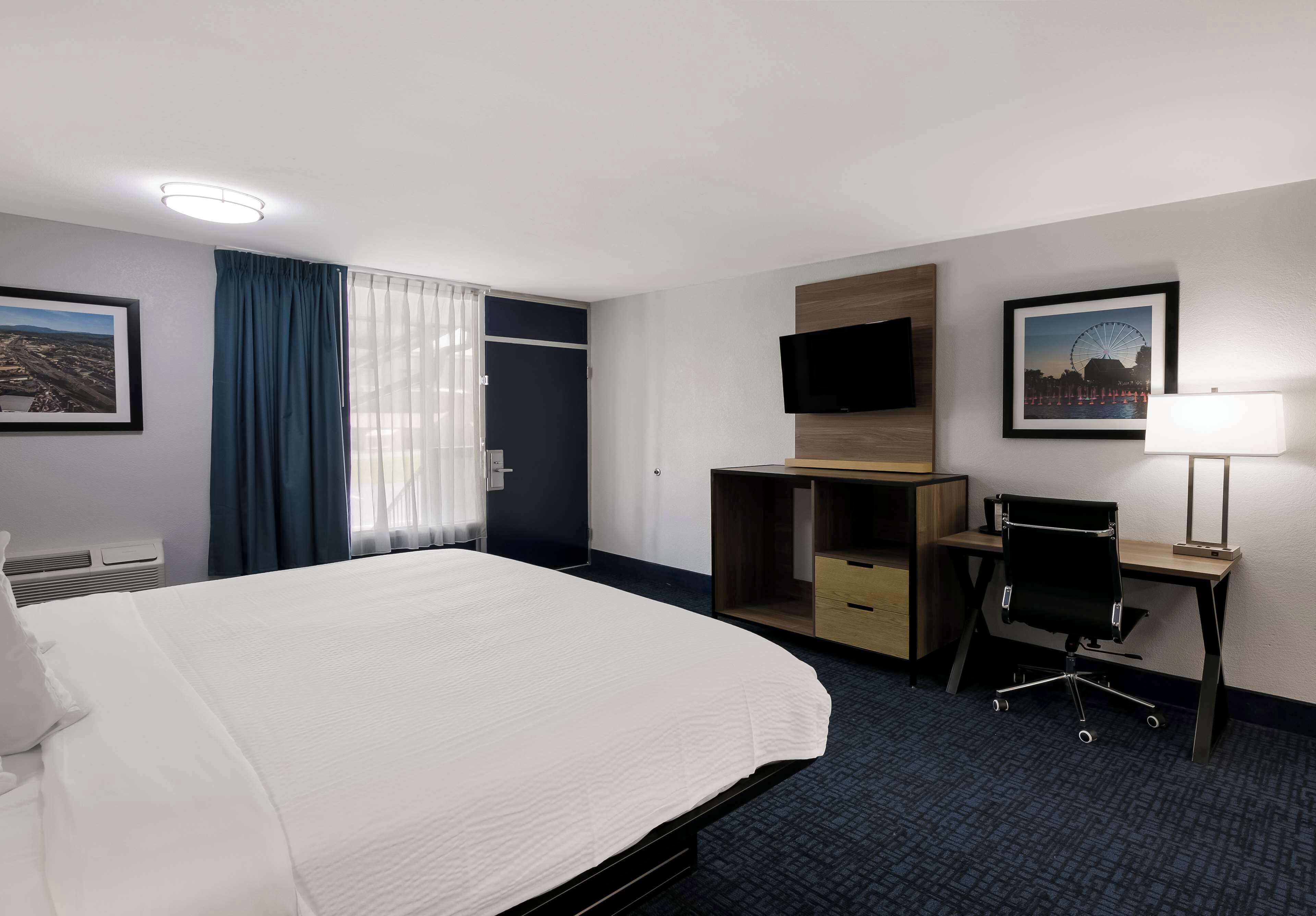 A hotel room with a large bed, a desk with a chair, a TV, and a window with curtains.