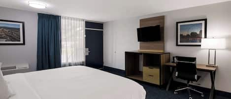 A hotel room with a large bed, a desk with a chair, a TV, and a window with curtains.