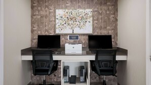 Un centro de negocios con dos escritorios, dos sillas, una impresora y un cuadro abstracto grande en la pared.