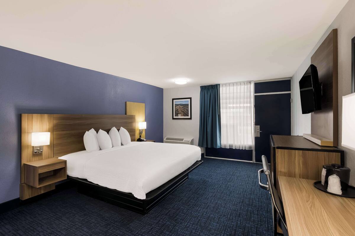 Een hotelkamer met een groot bed, nachtkastjes met lampen, een bureau met stoel, een televisie en een raam met gordijnen.
