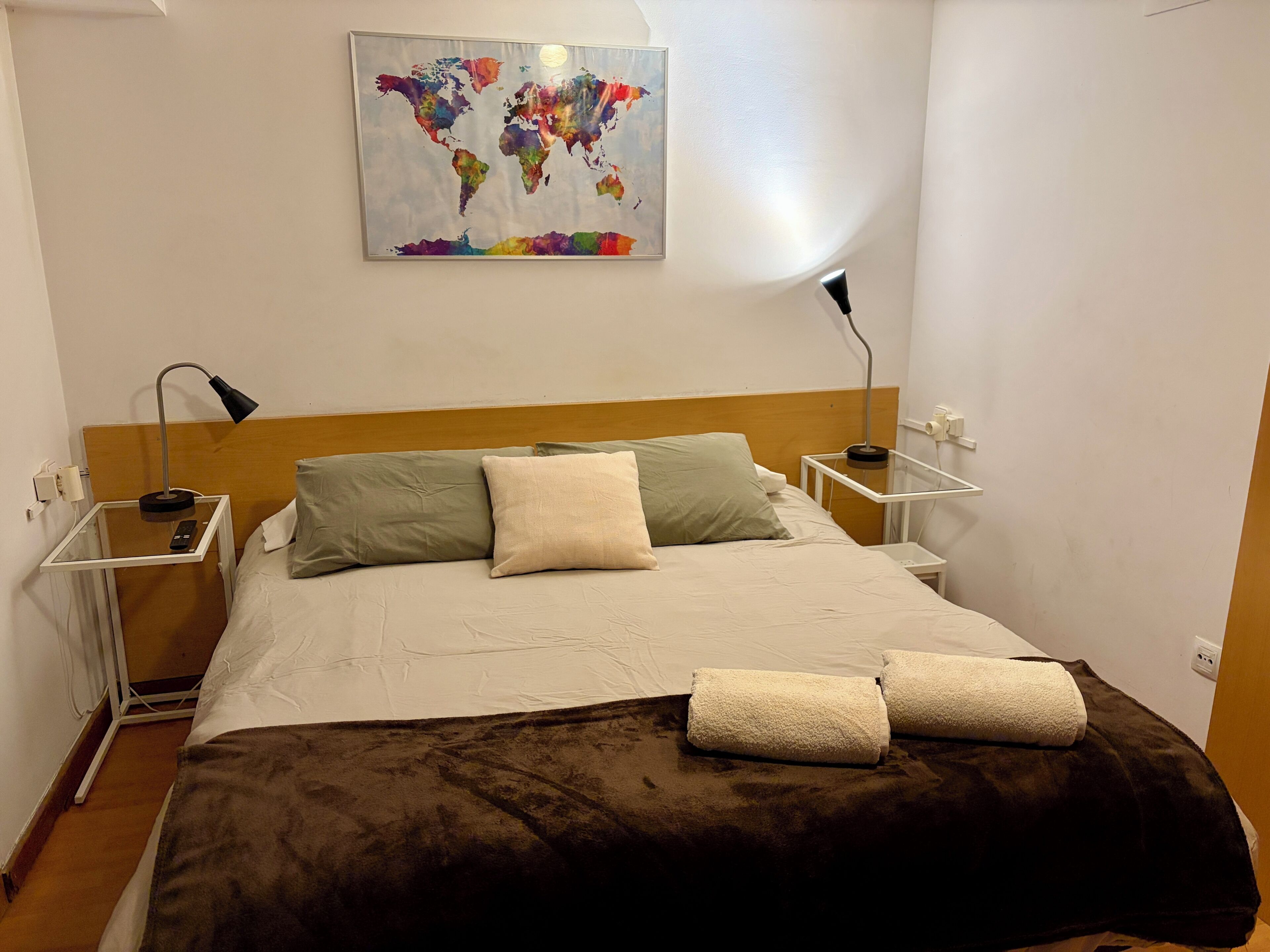 Een hotelkamer met een bed, kussens, een dekbed, een wereldkaart aan de muur en nachtlampjes.