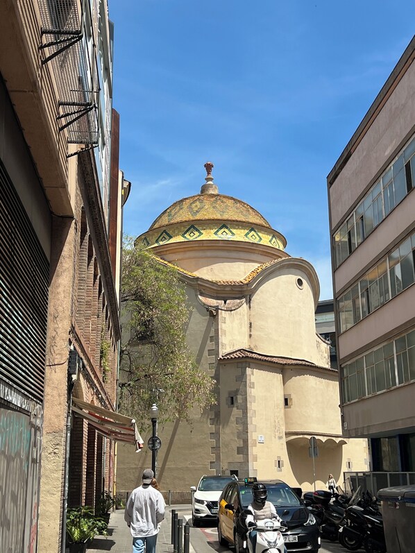A street with a historic building featuring a dome, a narrow alley, and parked vehicles. - Beautiful flat in the center only for you (Barcelona)