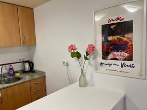 Cozinha com armários de madeira, bancada de granito, pia, chaleira e um vaso com flores cor-de-rosa.