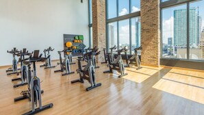 A gym with stationary bikes arranged in rows, a wall-mounted exercise board, and a view of the cityscape through large windows. - PRESTIGE PENTHOUSE W OCEAN VIEW BRICKELL (Miami)