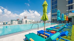 A rooftop pool with blue and green lounge chairs and umbrellas, surrounded by modern buildings and a clear sky. - PRESTIGE PENTHOUSE W OCEAN VIEW BRICKELL (Miami)