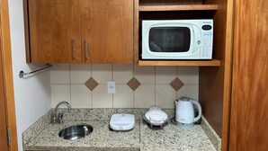A compact kitchen with wooden cabinets, a built-in microwave, a kettle, and a sink.